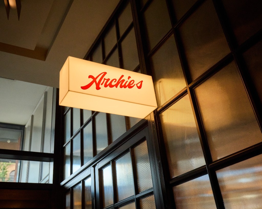 Illuminated Archie's sign mounted against black-framed textured glass panels
